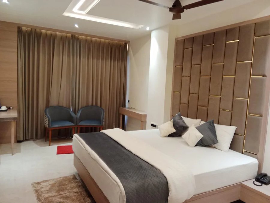 Guest room with curtains, armchairs and panelled headboard at Hotel Awadh Palace, Khurai